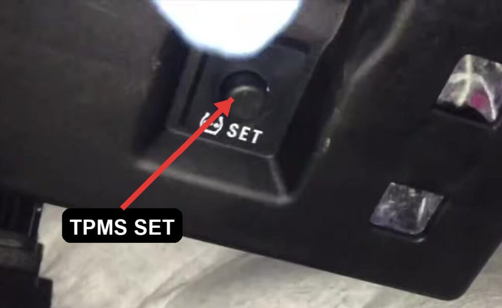 Toyota Yaris XP130 TPMS SET reset button under the lower dash, marked with the tire-pressure symbol and the word SET.