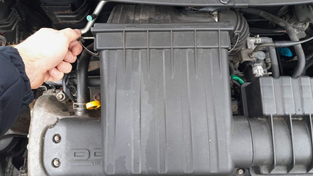 Air cleaner box on the Suzuki Swift 1.3 M13A, with a hand releasing the metal spring clip