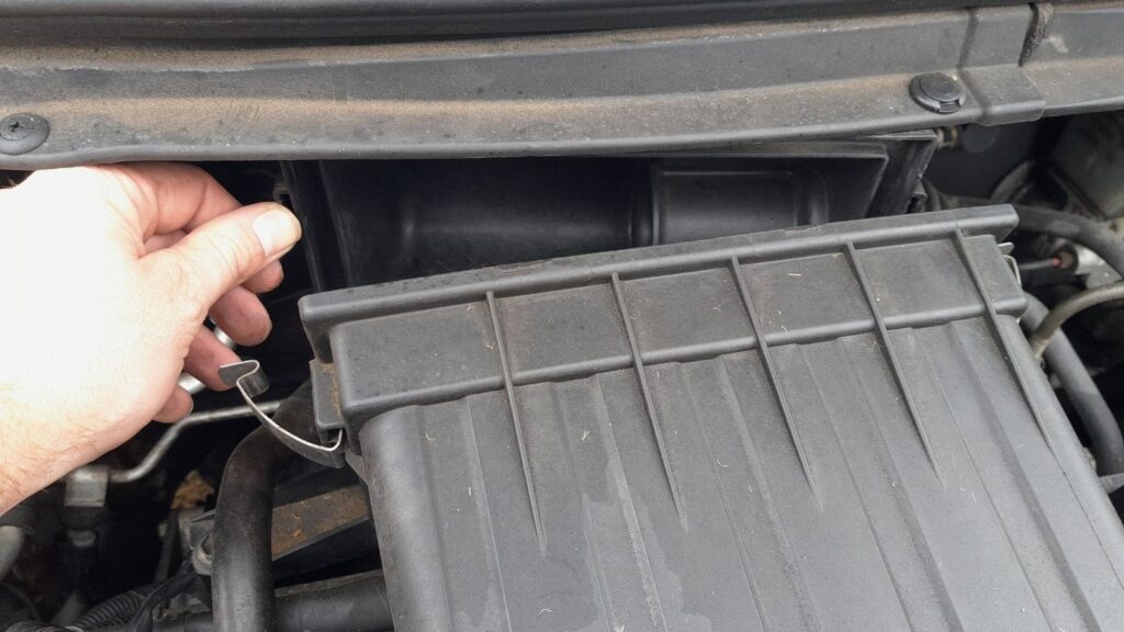 Releasing the wire spring clip that holds the Suzuki Swift air cleaner cover