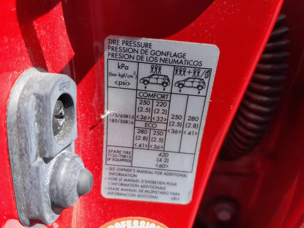 Suzuki Swift Mk3 tyre-pressure placard in the driver door jamb listing the recommended cold pressures.