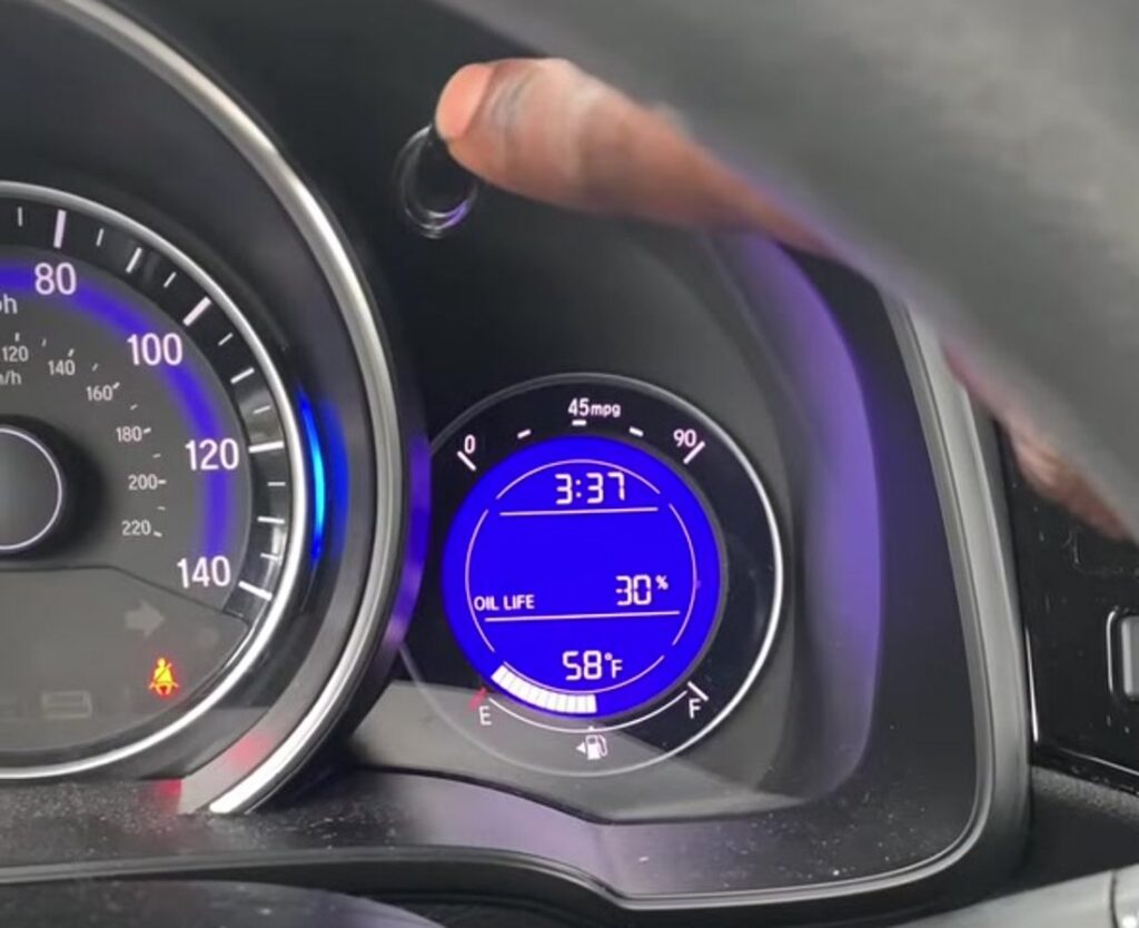Honda Jazz Mk3 (GK) / Fit instrument cluster showing the OIL LIFE 30% screen with a finger on the SEL/RESET button used to reset the service indicator.