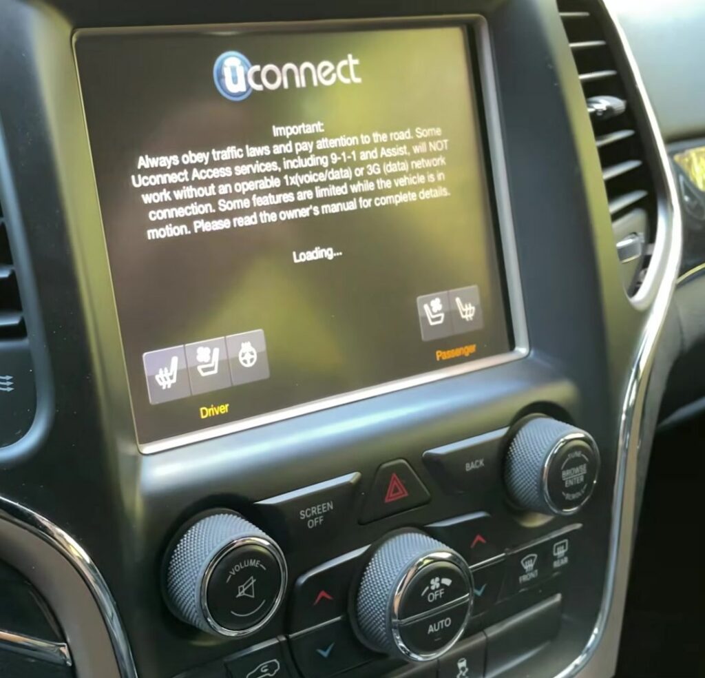 Jeep Grand Cherokee WK2 Uconnect touchscreen showing the Uconnect reboot loading splash, with the volume knob (lower left) and tune/browse-enter knob (right) below.