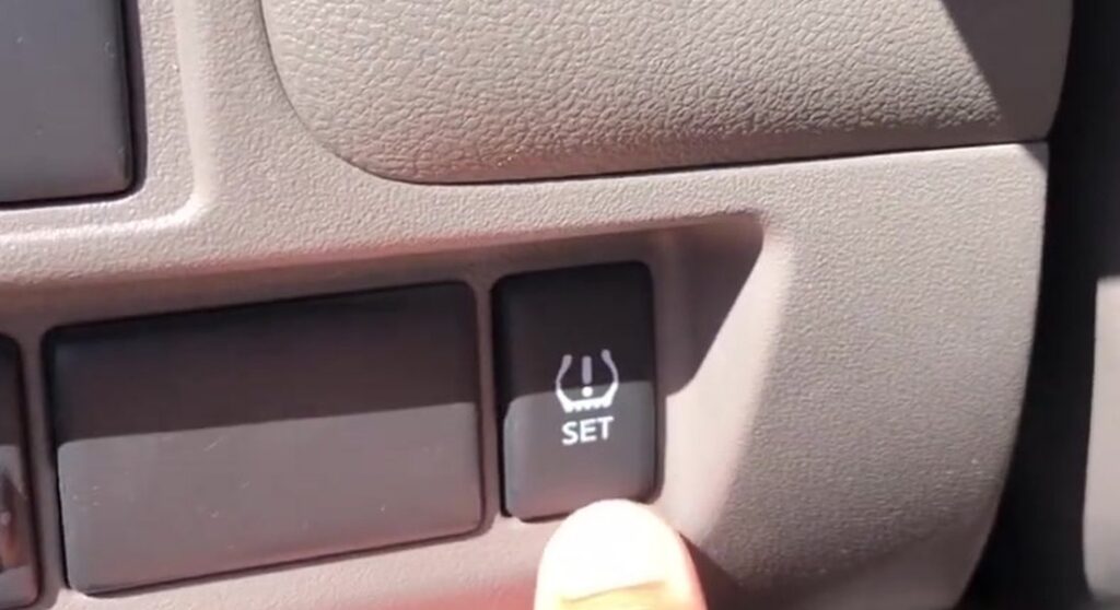 TPMS SET reset button on the lower dash of a Nissan Micra K13, marked with a tyre and exclamation symbol