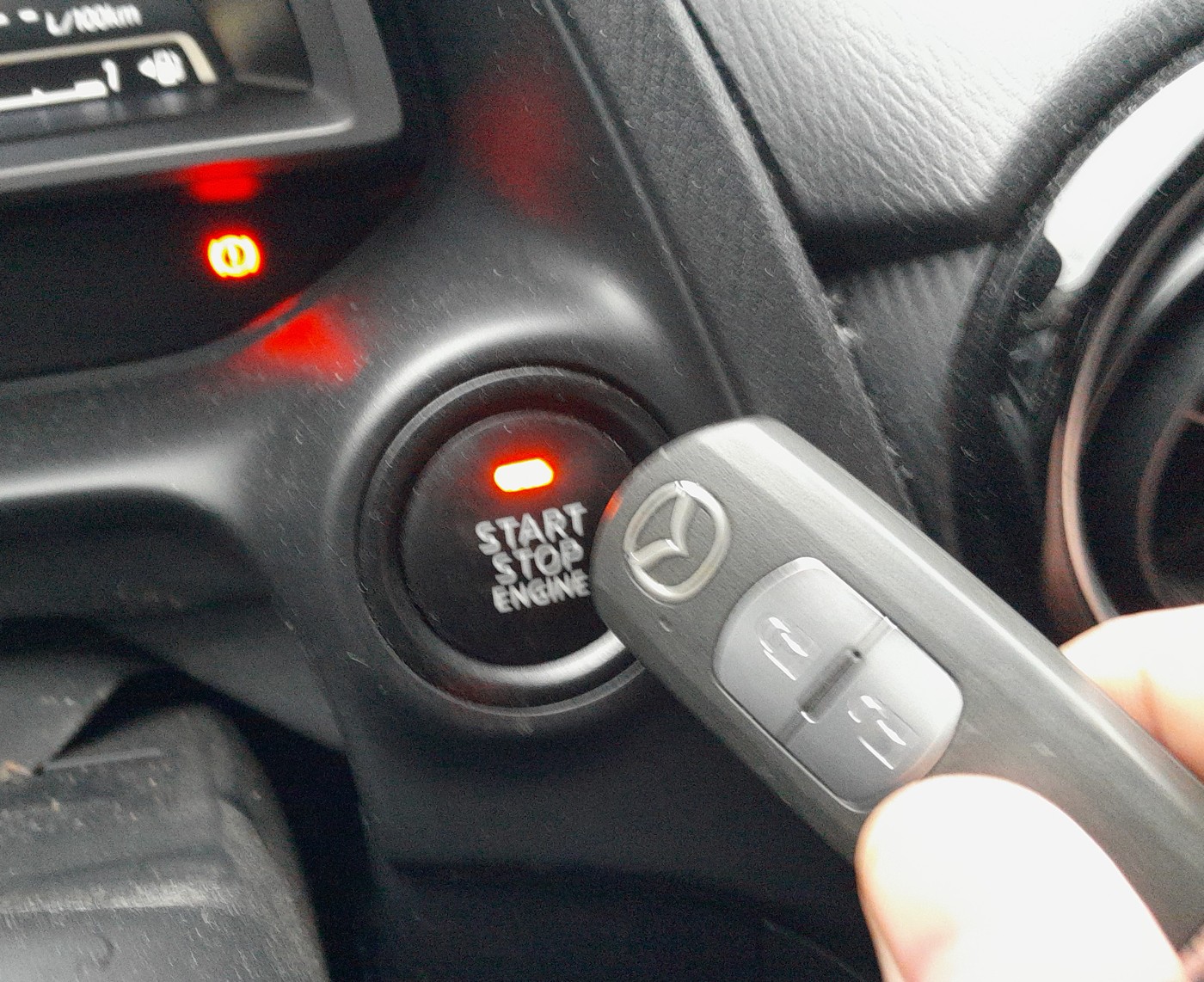 Mazda key fob held against the Start/Stop engine button on a Mazda 2 DJ