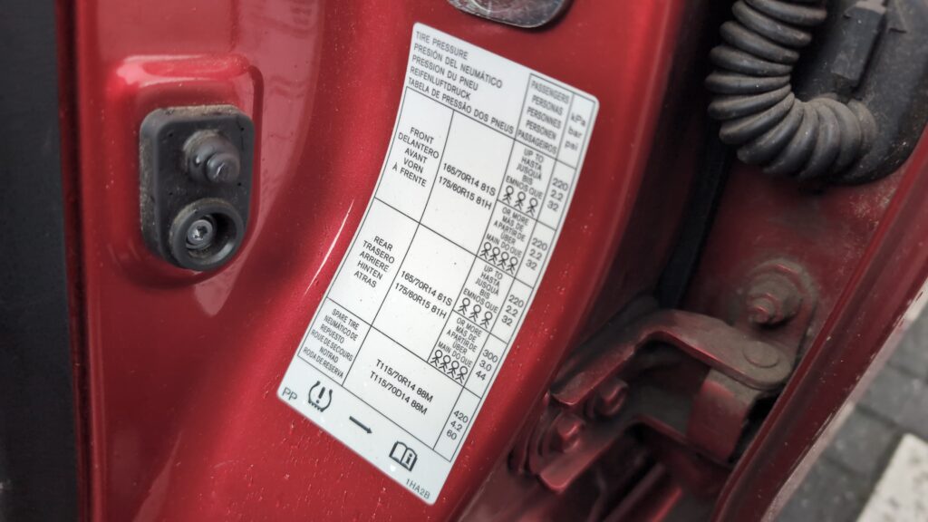 Nissan Micra K13 tyre pressure placard in the driver's door aperture showing recommended pressures.