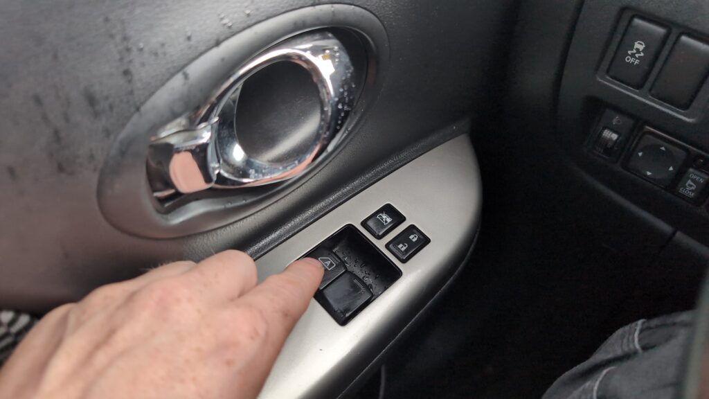 Nissan Micra K13 driver's door window switches, finger on the driver's window switch.