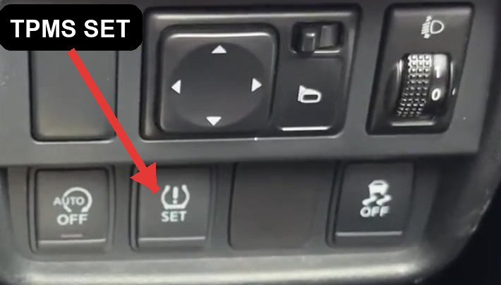 Nissan Juke F15 dashboard TPMS SET button (arrowed) in the lower switch panel below the steering wheel