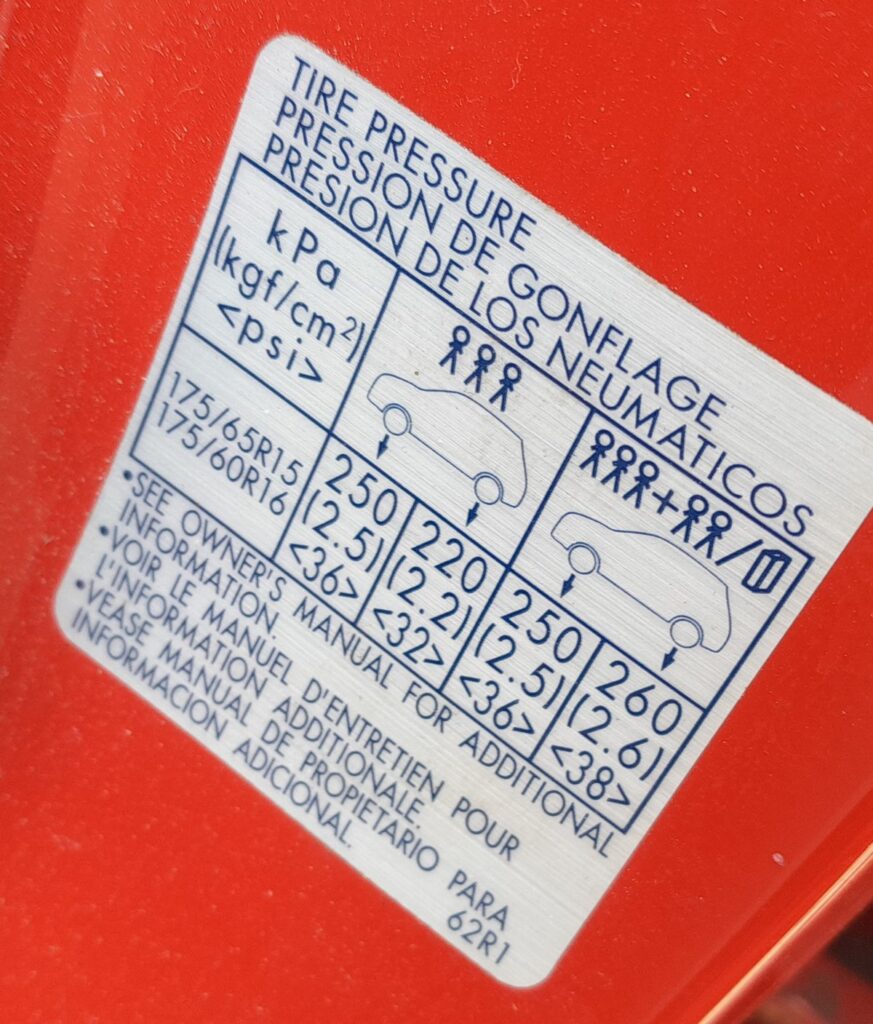 Suzuki Ignis tire-pressure placard in the driver door opening showing 175/65 R15 and 175/60 R16 pressures