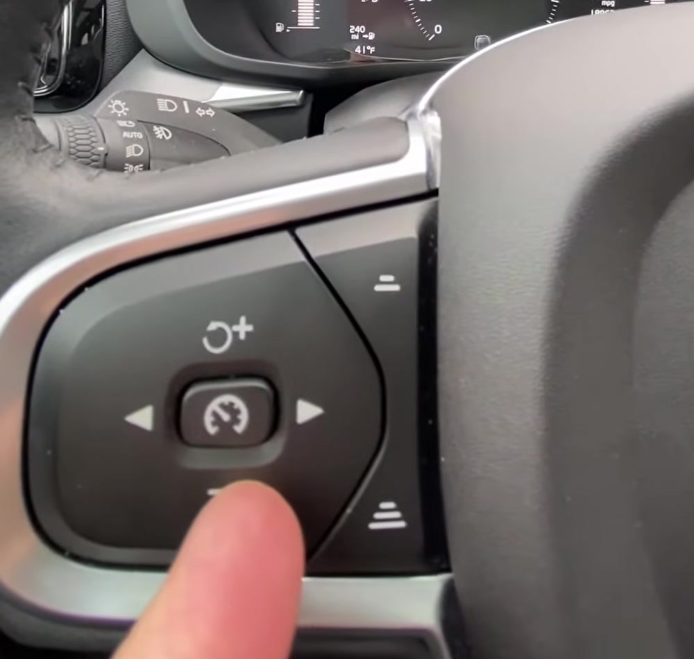 Volvo XC60 left steering-wheel keypad with a finger on the reduce cruise-speed minus button