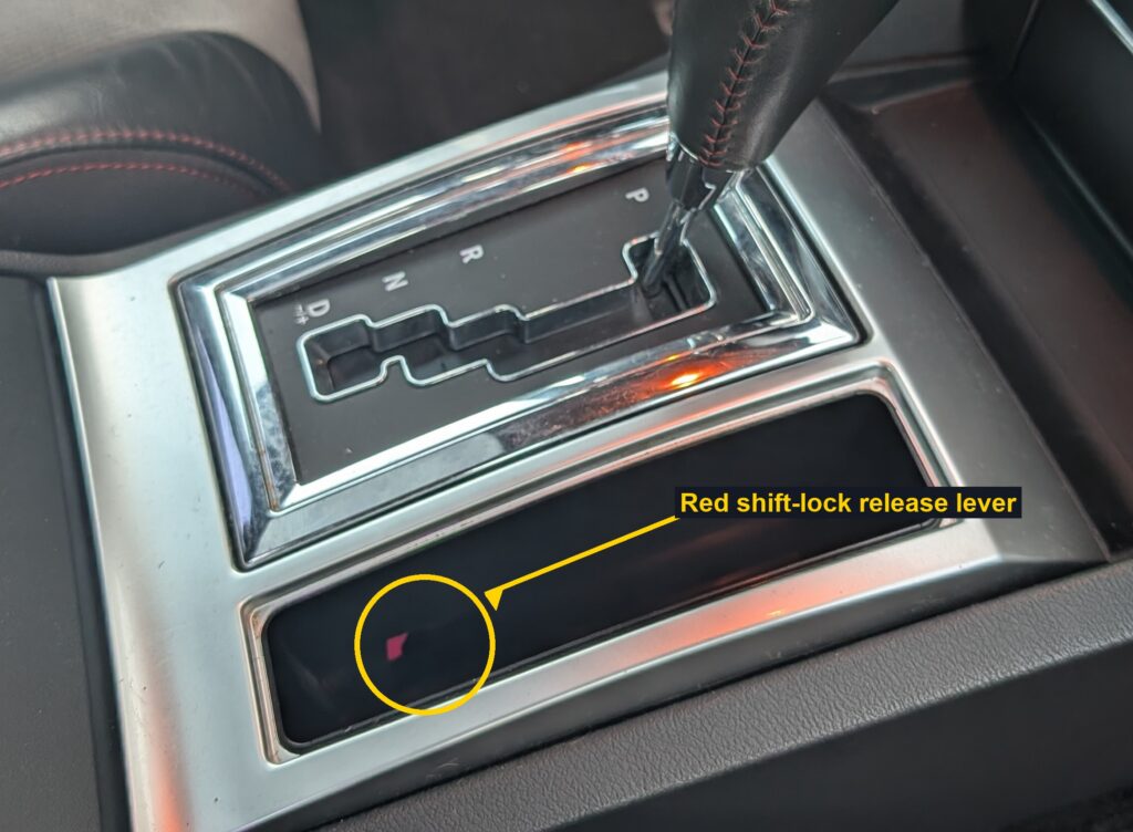Console gear selector on a Dodge Charger SRT8 with the red shift-lock release lever circled in the storage tray below