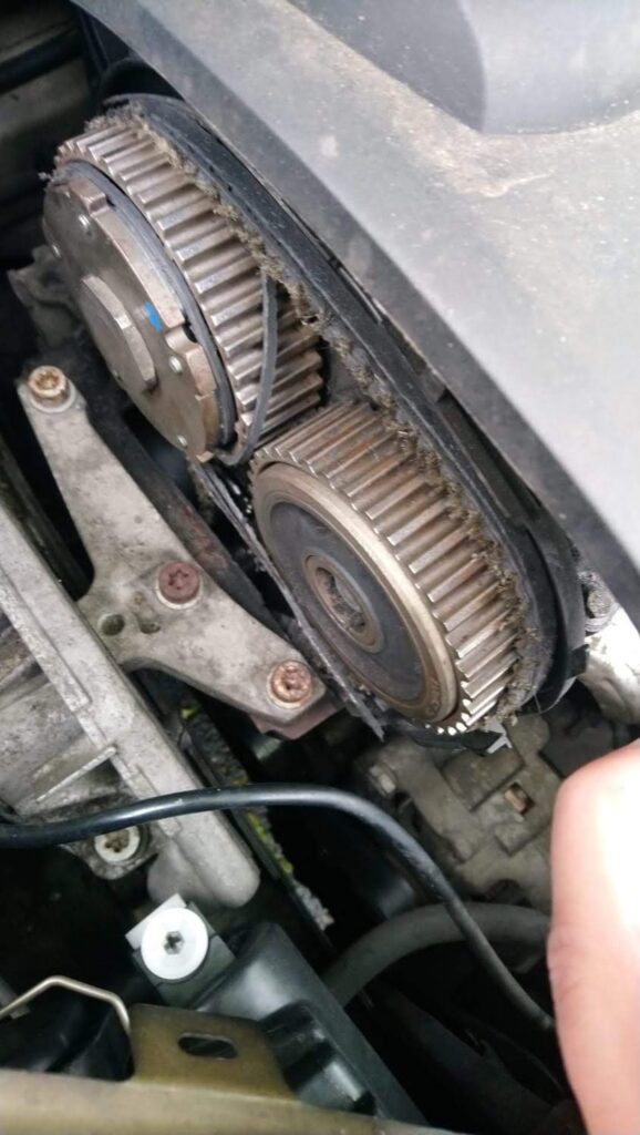 Twin camshaft timing-belt sprockets on a boxer engine with the belt in place and the alignment mark visible, showing signs of shedding