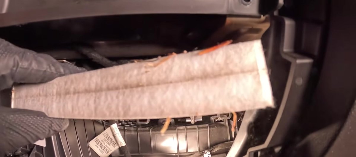 Old cabin air filter being pulled from its housing behind the lower glove box on a Chevrolet Silverado 1500 K2XX