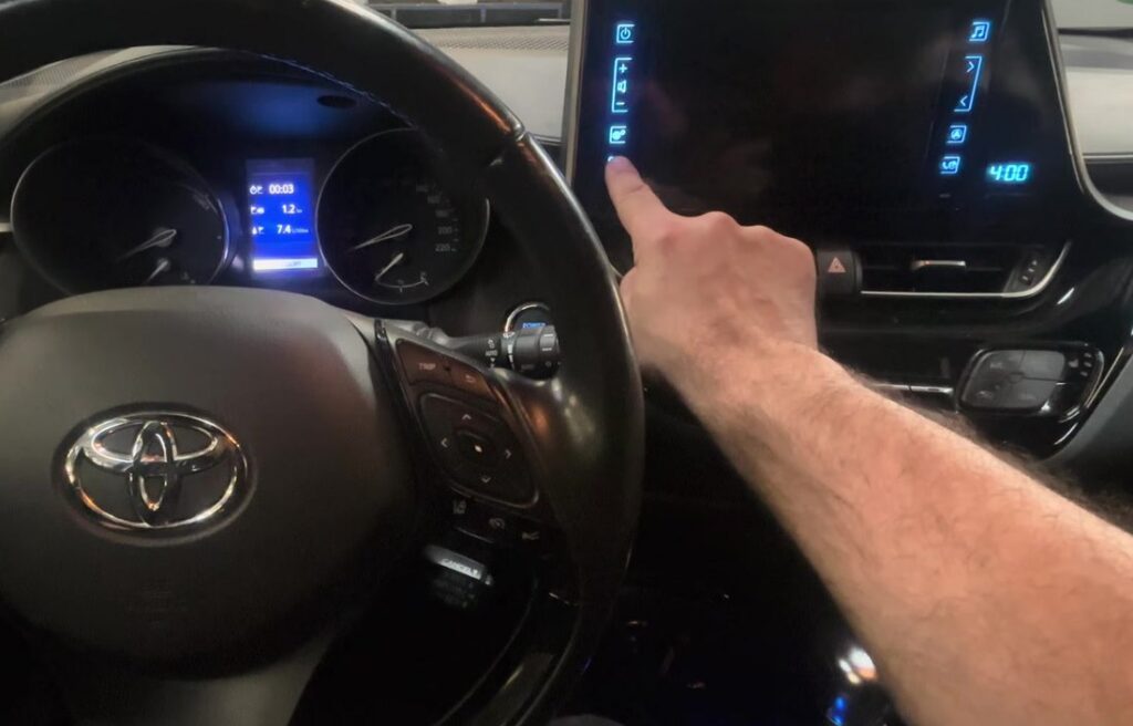 Finger pressing the settings gear icon on the left touch column of a Toyota C-HR Display Audio, cluster in ACCESSORY mode