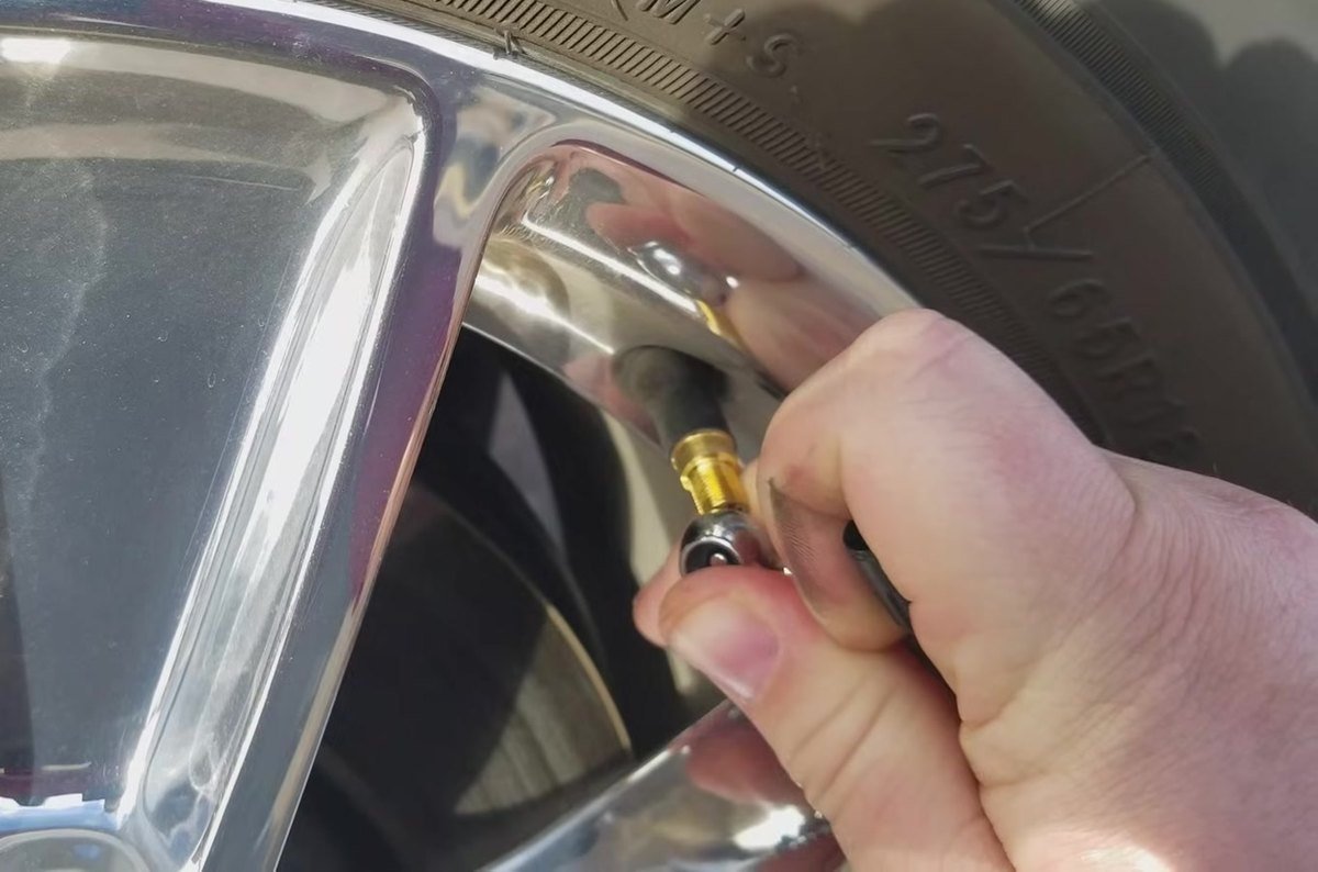 A hand briefly bleeding air from a Ford F-150 tyre valve stem during the TPMS relearn