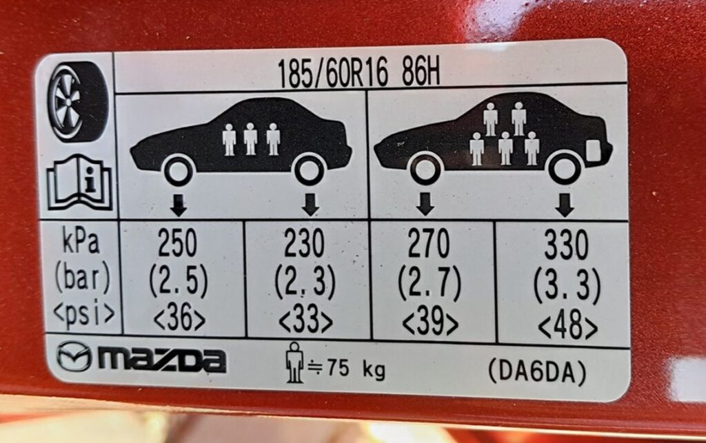Tire-pressure placard on a Mazda 2 DJ driver's door pillar showing 185/60 R16 pressures