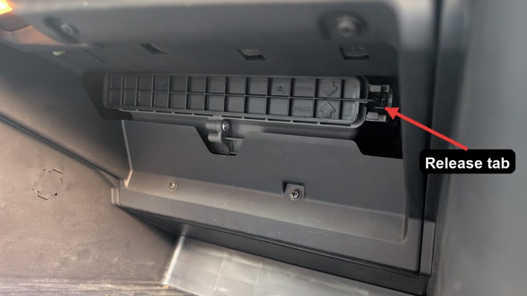 Kia Rio cabin filter cover with OPEN arrows and the release tab marked
